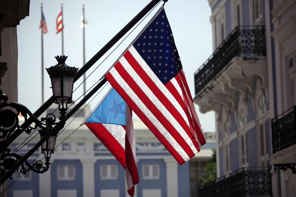 FILE - In this June 29, 2015 file photo, U.S. and Puerto Rico flags hang outside the governor’s mansion in Old San Juan, Puerto Rico. Puerto Rico's power company said Wednesday, Sept. 2, 2015 it reached an agreement with a group of bondholders to restructure the troubled agency, providing some relief to investors who believed it soon would go bankrupt. The bondholders hold about 35 percent of the power company's bonds and represents hedge funds and municipal bond investors. (AP Photo/Ricardo Arduengo, File)